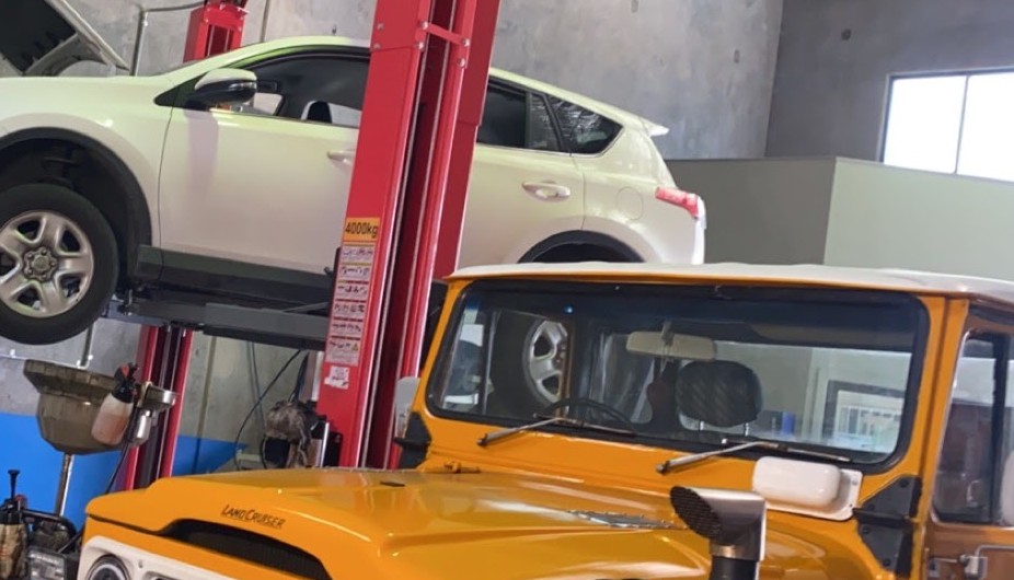 The Jimboomba Autocare workshop floor with a Toyota RAV4 on the red hoist and a restored orange Land Cruiser alongside